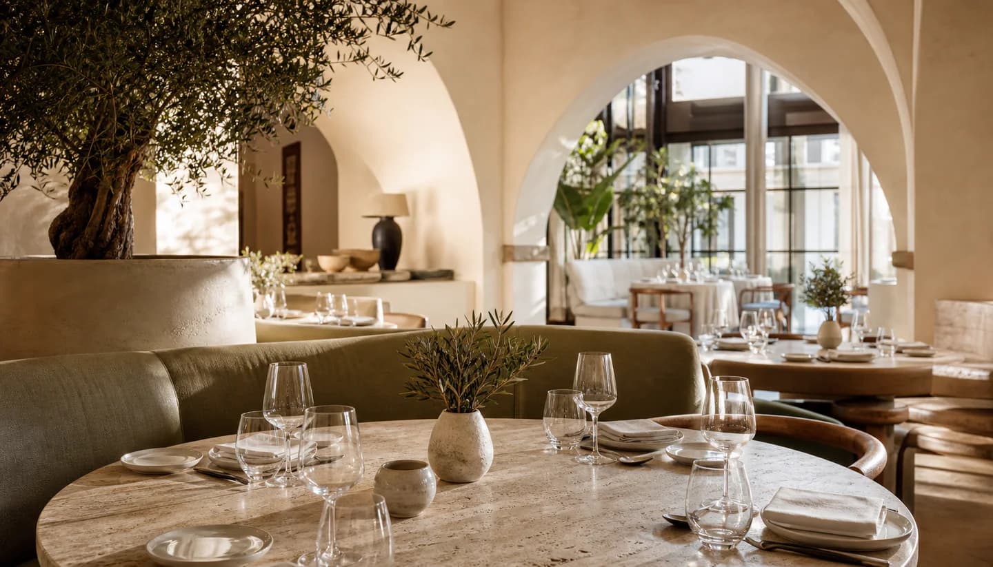 Sunlit cream restaurant with olive trees and curved archways